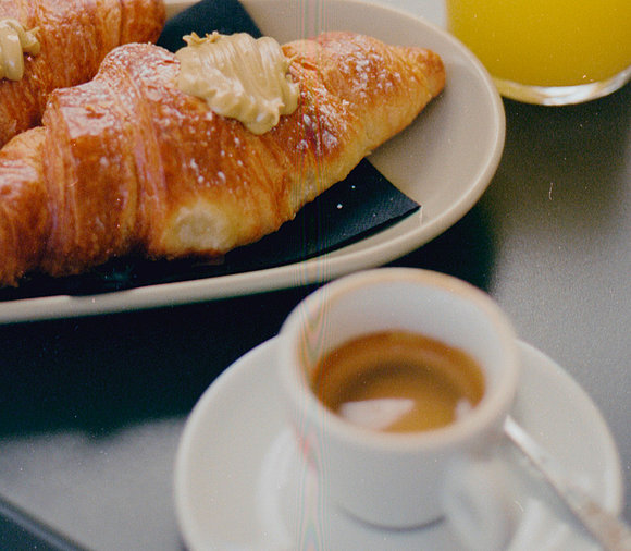 Auf dem Bild ist eine Espressotasse sowie ein Teller mit einem Croissant abgebildet. 