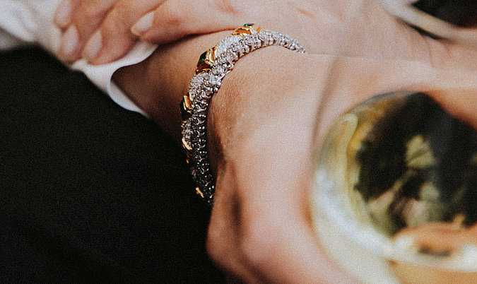 Man erkennt eine Hand, die ein Weissweinglas in der Hand hält. Am Handgelenk trägt sie Schmuck.