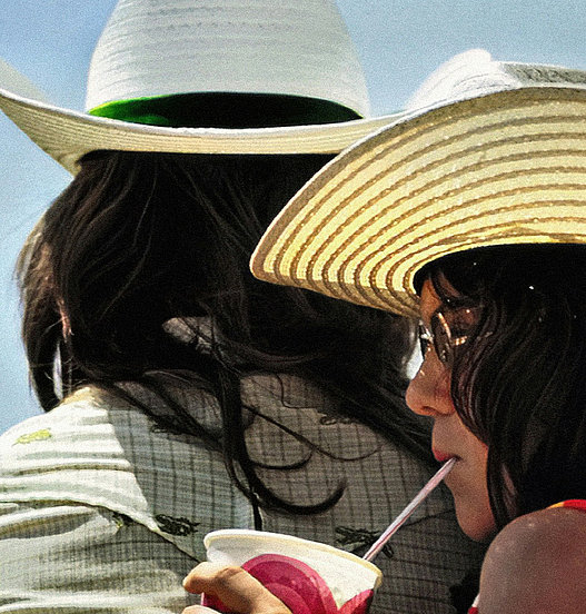 Zwei Personen mit Sonnenhüten genießen ein Getränk im Freien an einem sonnigen Tag.