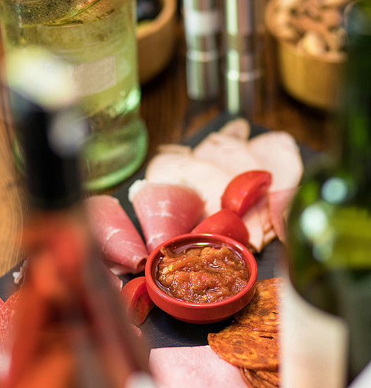 Auswahl an Antipasti mit Aufschnitt, Dip und Knabbergebäck auf einem gedeckten Tisch.