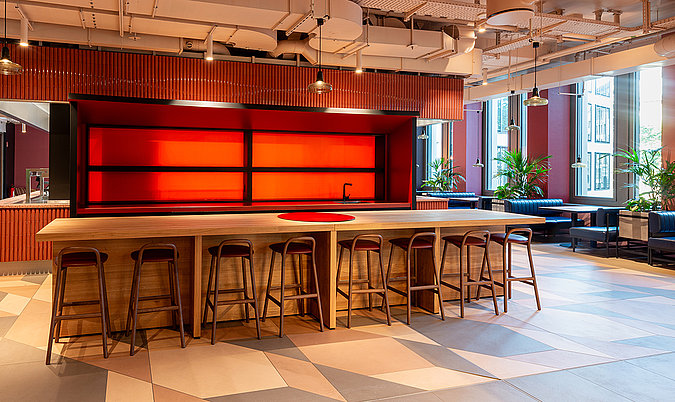 Zentraler Bartresen mit Barhockern, roter Hintergrundbeleuchtung und modernem Restaurantambiente.