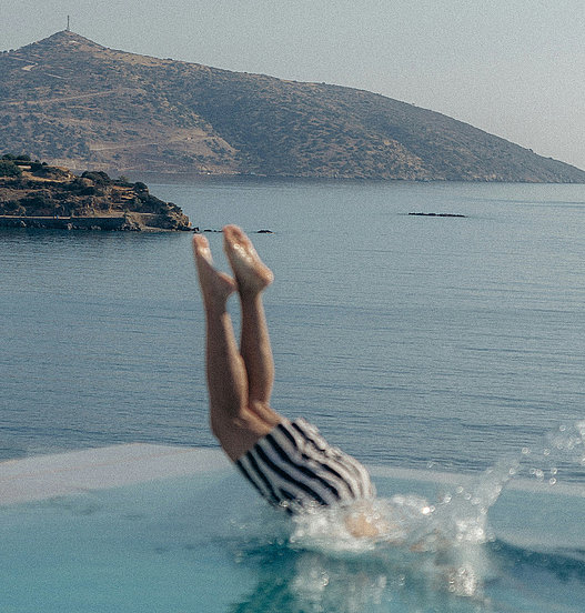 Person springt kopfüber in einen Pool mit Blick auf das Meer und die Küstenlandschaft.