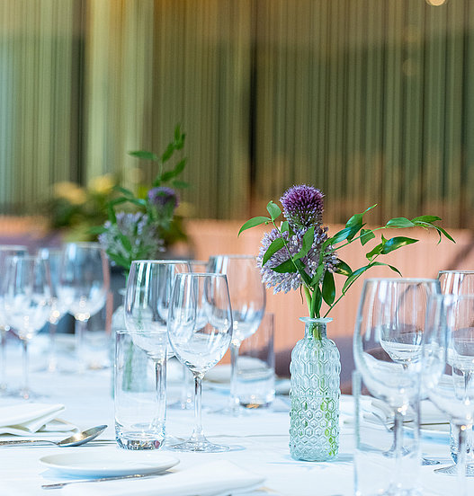 Lange Banketttafel mit Gläsern und dezenten Blumenvasen.