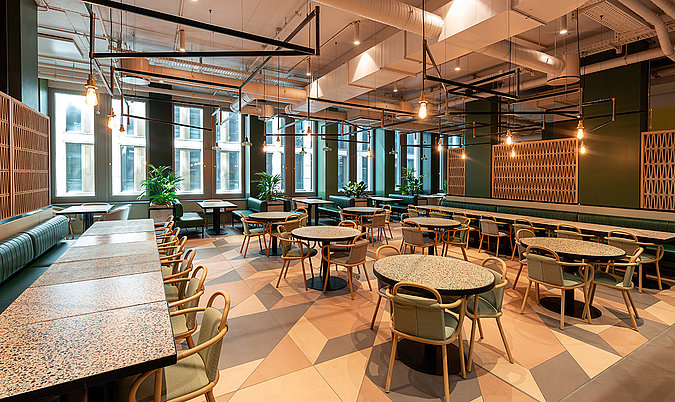 Moderner Restaurant- und Eventbereich mit runden und langen Tischen, Sitzbänken und offenem Raumkonzept.