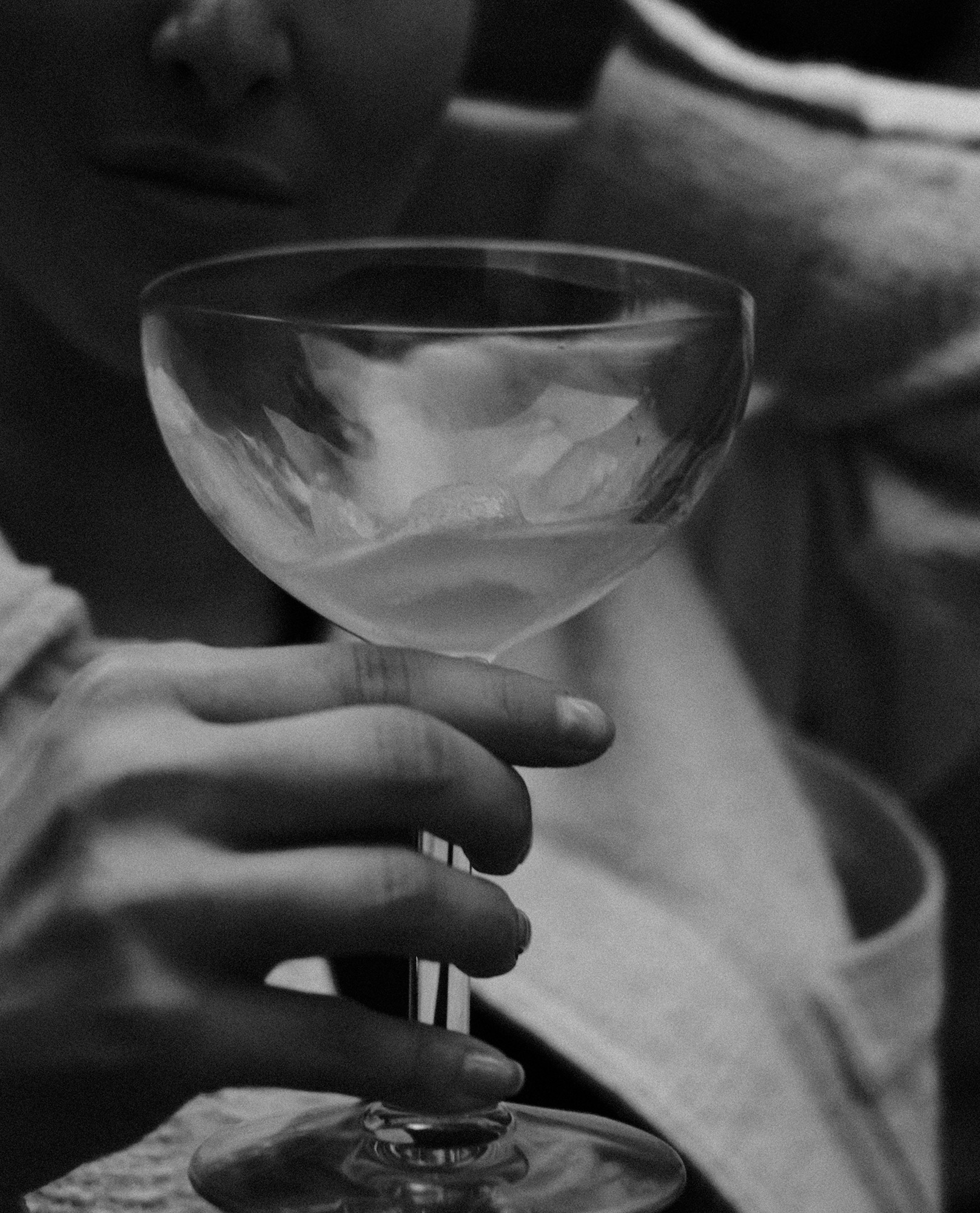 Hand hält eine Cocktailschale mit Eiswürfeln in stilvollem Schwarz-Weiß-Ambiente.